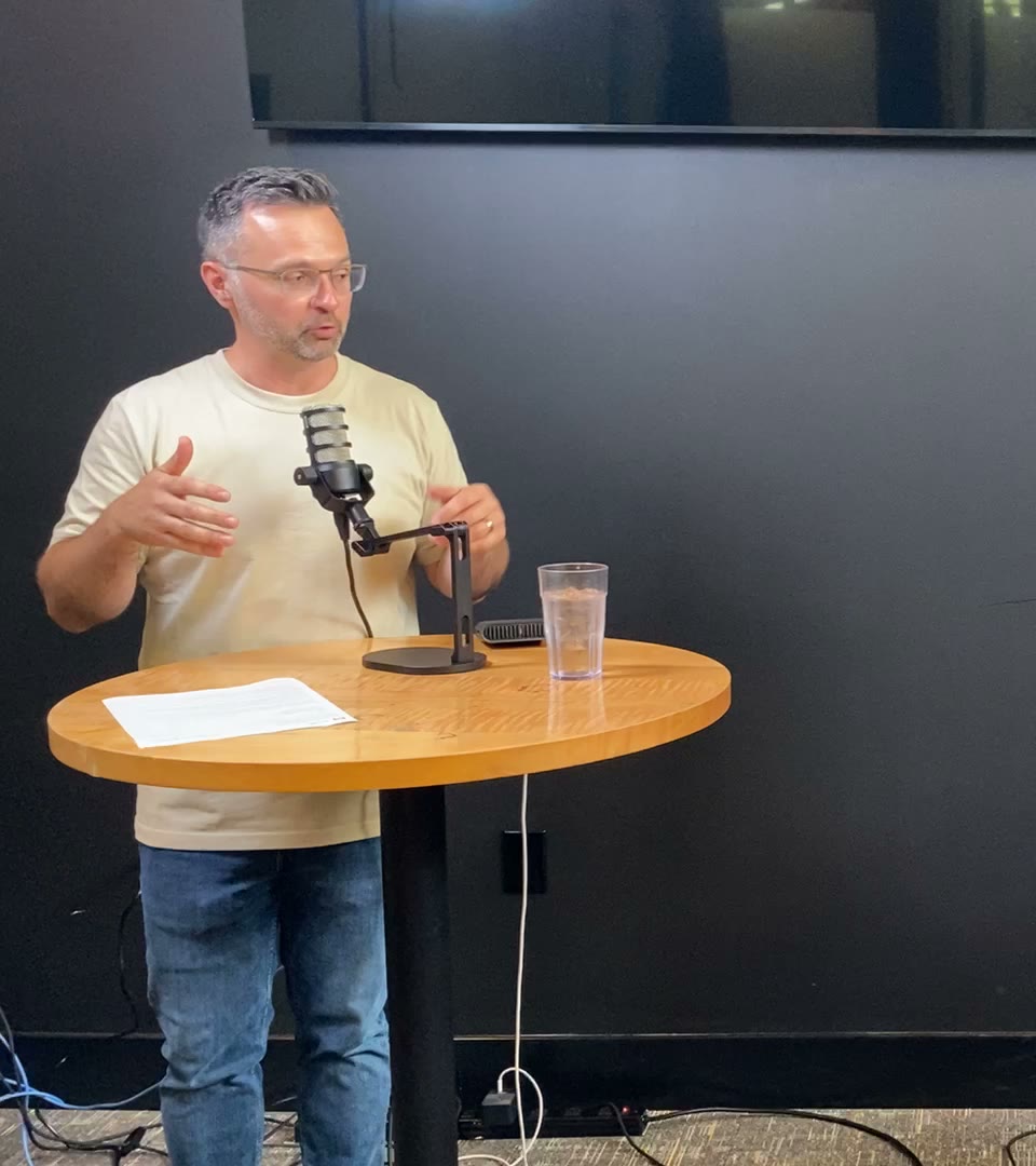 Andrew Witchell speaking at a table with a microphone